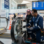 Foreign technicians and maintenance workers in Saudi Arabia travel sector inspecting airport equipment and performing repair tasks in a modern transport facility.